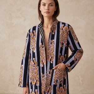 Könnte beinhalten: Gesteppte Jacke mit Tigerprint in Orange und Rosa, vor vertikalen schwarzen und hellblauen Streifen. Die Jacke hat eine lockere Passform, lange Ärmel und zwei Vordertaschen. Ein stilvolles Kleidungsstück.