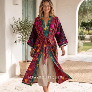 Puede incluir: Un kimono vibrante con estampado floral en tonos rojos, rosas y amarillos, con un ribete verde turquesa. El kimono se ata a la cintura con un cinturón a juego. El texto "NAAZBOUTIQUE01" es visible.