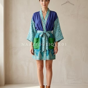 May include: A knee-length robe with a blue top and sleeves, and a green and blue patterned skirt. The robe has a matching belt and pockets. The text "NAAZ BOUTIQUE 01" is printed on the front of the robe.
