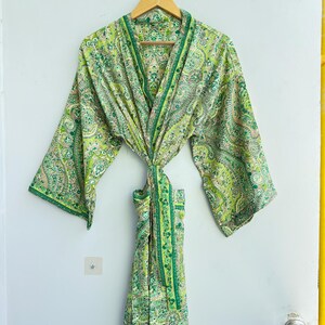 May include: A lightweight robe featuring a vibrant green and white paisley pattern. The garment has wide, three-quarter length sleeves, a shawl collar, and a matching fabric tie belt at the waist. The intricate print covers the entire surface.