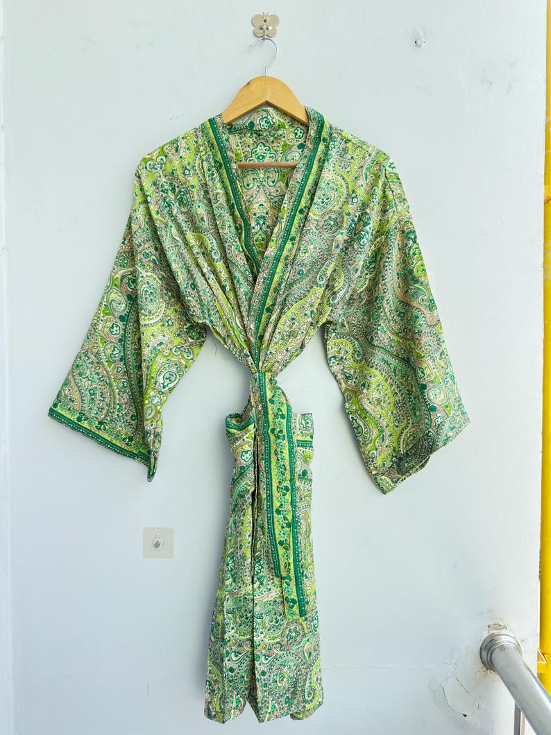 May include: A lightweight robe featuring a vibrant green and white paisley pattern. The garment has wide, three-quarter length sleeves, a shawl collar, and a matching fabric tie belt at the waist. The intricate print covers the entire surface.