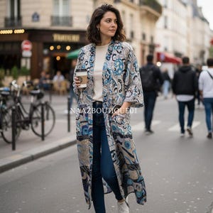 Könnte beinhalten: Ein langer, gemusterter Kimono in Blau-, Beige- und Schwarztönen, getragen über einem weißen Oberteil und dunkelblauen Jeans. Der Kimono hat ein kompliziertes Paisley-Design. Das Outfit wird mit weißen Turnschuhen abgerundet. Der Text "NAAZBOUTIQUE01" ist sichtbar.