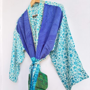 May include: A colorful, patterned robe with a blue and white floral design. The robe features a solid blue panel across the shoulders and a matching tie. The sleeves are long and the robe is hanging on a wooden hanger.