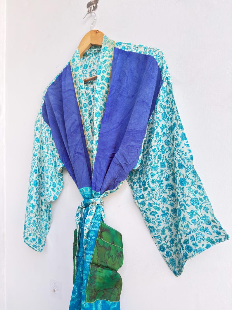 May include: A colorful, patterned robe with a blue and white floral design. The robe features a solid blue panel across the shoulders and a matching tie. The sleeves are long and the robe is hanging on a wooden hanger.
