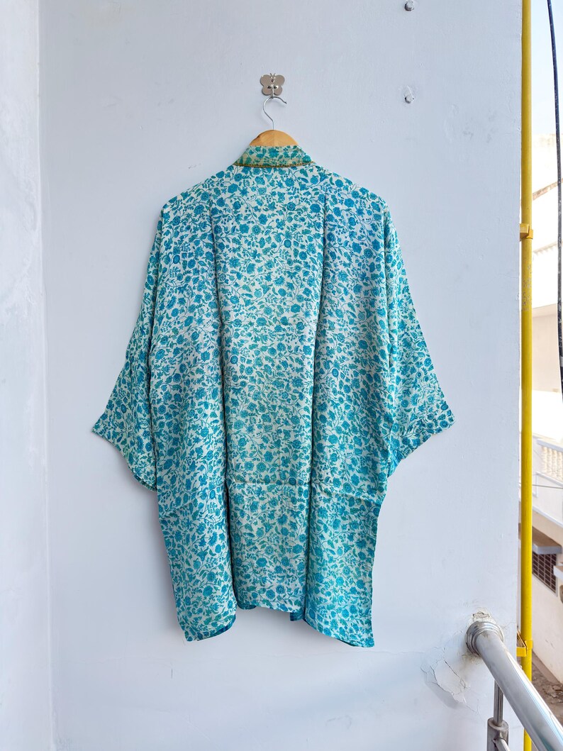May include: A blue and white floral patterned kimono-style robe hanging on a wooden hanger. The robe has a loose, flowing design with wide sleeves. The floral pattern is a mix of small blue flowers on a white background.