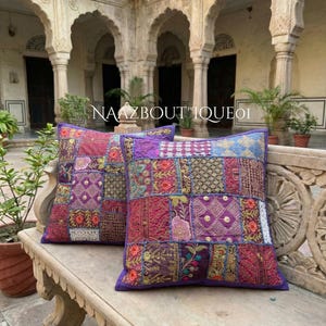 Könnte beinhalten: Zwei quadratische Zierkissen mit Patchwork-Design. Die Kissen weisen eine Vielzahl von Stoffen in Lila-, Rot- und Goldtönen mit gestickten Blumen- und geometrischen Mustern auf. Der Text "NAAZBOUTIQUEOI" ist sichtbar.