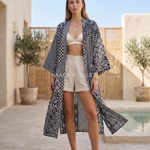 Könnte beinhalten: Ein langer, gemusterter Kimono in Schwarz und Weiß. Der Kimono hat verschiedene geometrische Muster und wird mit einem weißen Oberteil und Shorts getragen. Das Bild wird im Freien bei natürlichem Licht aufgenommen.