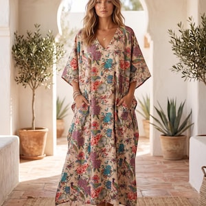 Könnte beinhalten: Beige Kaftankleid mit floralem Muster, V-Ausschnitt und Taschen. Das Kleid zeigt ein farbenfrohes Muster aus Blumen und Vögeln in Rot-, Blau- und Lilatönen. Der Text "NAAZBOUTIQUE01" ist unten sichtbar.