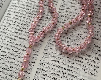 May include: A pink and gold rosary with a cross charm. The rosary beads are made of glass and have a sparkly finish. The cross charm is made of gold and has a pearl center.