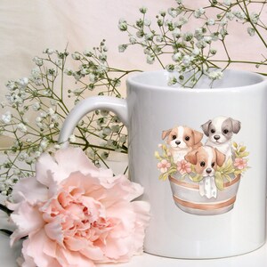 May include: White ceramic mug with a colorful illustration of three puppies in a flower pot. The puppies are brown, white, and black with brown spots. The pot is gray with white stripes and has pink flowers around it.