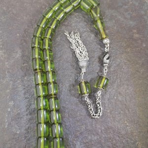 May include: A green and silver prayer bead set. The beads are rectangular and translucent, with a lighter green stripe down the center. The silver components include a tassel and decorative end pieces. The beads are strung on a green cord.