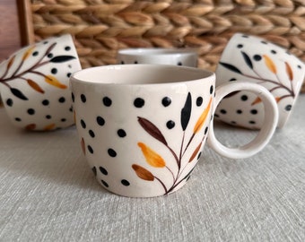 May include: Set of four white ceramic coffee mugs with black polka dots and a brown and yellow floral design.
