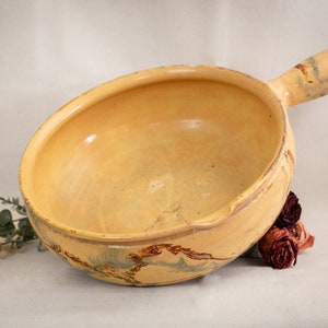 May include: A large, yellow ceramic bowl with a handle. The bowl has a rustic, hand-painted design with brown and blue accents.