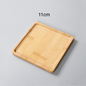 May include: A square, light brown bamboo tray with a raised edge. The tray measures 11 inches across.