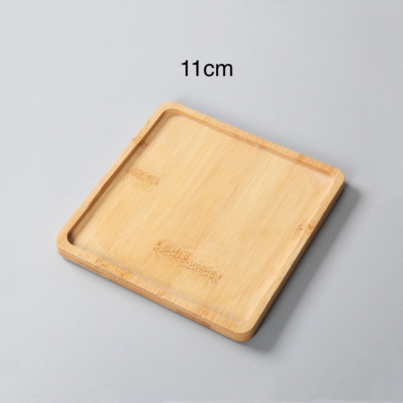 May include: A square, light brown bamboo tray with a raised edge. The tray measures 11 inches across.