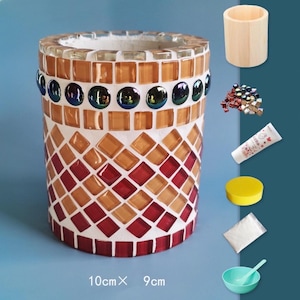 May include: A mosaic art kit with a cylindrical vase, measuring 10cm x 9cm, in shades of red, orange, and white. The kit includes a wooden cup, mosaic tiles, glue, a sponge, a bag of powder, and a small bowl with a spoon.
