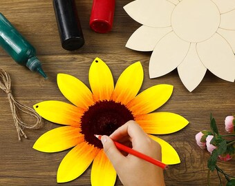 May include: A wooden sunflower craft with yellow petals and a brown center. The sunflower is being painted with a red pencil. The craft is on a wooden surface with paint bottles and a blank wooden sunflower.