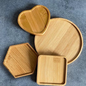 May include: Four wooden coasters in different shapes: heart, round, hexagon, and square. The coasters are made of light brown bamboo.