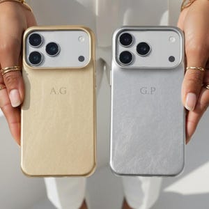 May include: Two personalized phone cases, one gold and one silver, are held up. The gold case has the initials "A.G." and the silver case has "G.P." Both cases have a camera module at the top. The cases are from the brand "iX Cases."