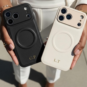 May include: Two personalized phone cases, one black and one cream, are held up. The black case has the initials "G.P." in gold, while the cream case has "L.T." in gold. Both cases have a circular design on the back.