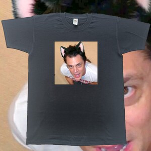 May include: Dark gray t-shirt featuring a square image of a person wearing cat ears. The person in the image is also wearing cat ears. The t-shirt is a crew neck style.