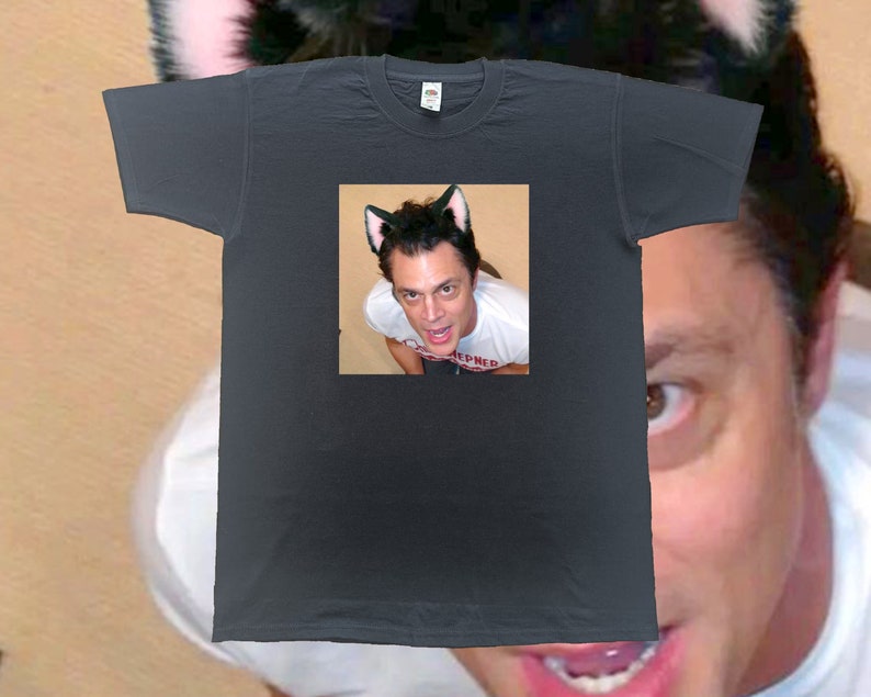 May include: Dark gray t-shirt featuring a square image of a person wearing cat ears. The person in the image is also wearing cat ears. The t-shirt is a crew neck style.