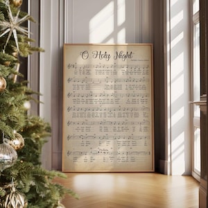 以下が含まれることがあります： 「O Holy Night」のクリスマスキャロルのヴィンテージスタイルのプリントで、楽譜と歌詞が書かれています。プリントはシンプルな茶色のフレームで額装され、白い壁に掛けられています。