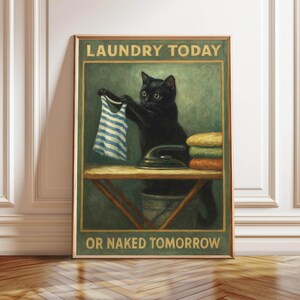 May include: A framed vintage-style print featuring a black cat holding a blue and white striped shirt. The cat stands near an ironing board with an iron and folded clothes. The text reads "LAUNDRY TODAY OR NAKED TOMORROW."