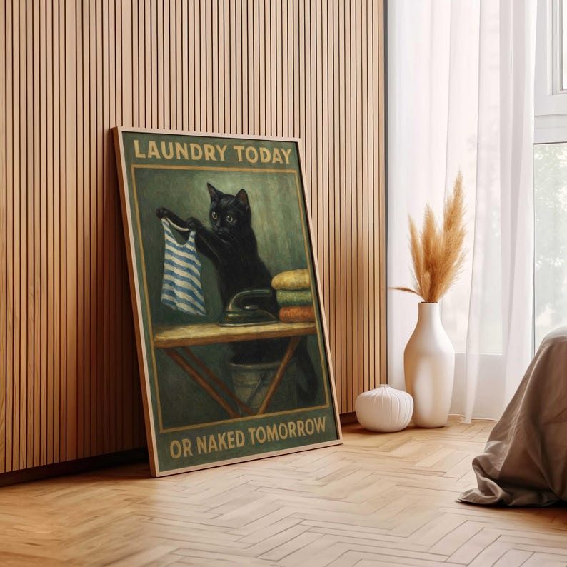 May include: Framed wall art featuring a black cat holding a blue and white striped shirt, with an iron and folded towels on a table. The text reads "LAUNDRY TODAY OR NAKED TOMORROW" in a vintage style.