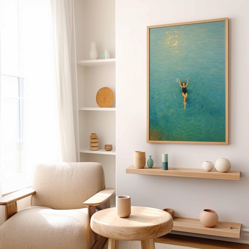May include: A framed art print depicts a person swimming in turquoise water. The artwork is in a light wood frame and hangs on a white wall. The room features a neutral color palette with wooden furniture and decorative vases.