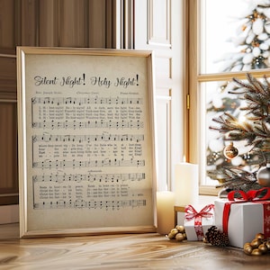 May include: A framed print of the Christmas carol "Silent Night! Holy Night!" with musical notes and lyrics. The print is in a gold frame and is displayed near a window with a Christmas tree and wrapped gifts.