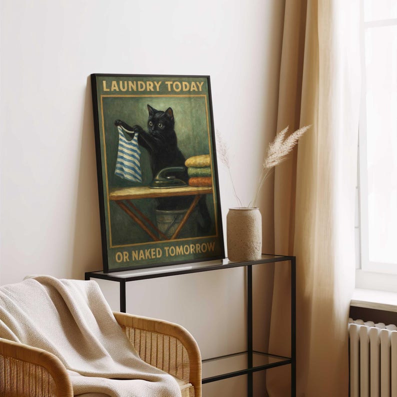 May include: A framed poster featuring a black cat ironing clothes with the text "LAUNDRY TODAY OR NAKED TOMORROW." The cat is holding a blue and white striped shirt. The poster is displayed on a black metal table.