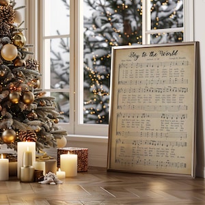 May include: A framed print of the hymn "Joy to the World" with musical notes and lyrics, displayed on a wooden floor. A decorated Christmas tree with gold ornaments and candles are in the background. The frame is a light brown color.