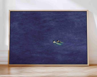 May include: A framed art print featuring two figures swimming in deep blue water. The artwork has a minimalist style, with the figures appearing small against the vastness of the water. The frame is a light wood color.