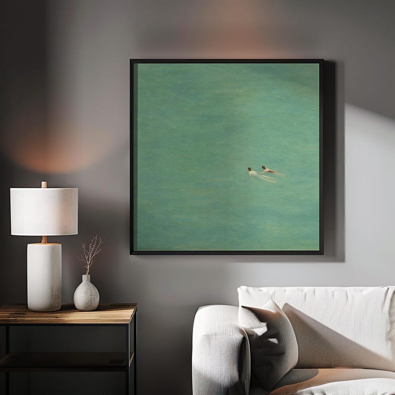 以下が含まれることがあります： ターコイズブルーの海で泳ぐ2人の姿を描いた額入りのアートプリント。アートワークは、白いソファの上にある灰色の壁に飾られています。白いランプと小さな花瓶が木製のサイドテーブルに置かれています。