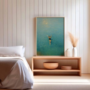 May include: A framed art print depicts a person swimming in turquoise water. The artwork is displayed above a wooden console table with decorative vases, a wooden bowl, and plates. The room features a bed with white linens and a neutral color palette.