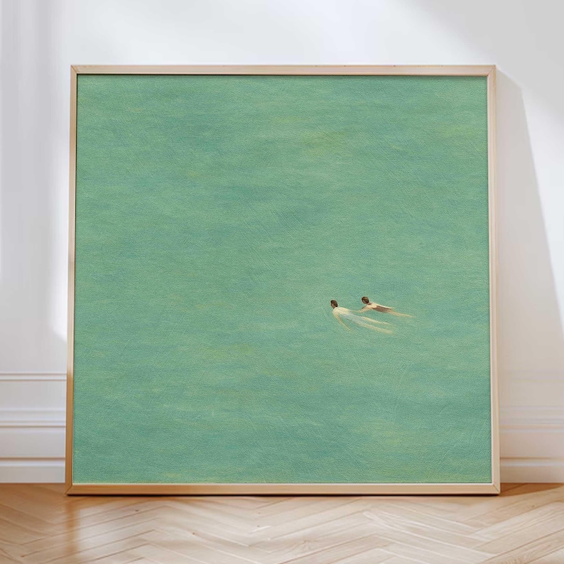 以下が含まれることがあります： ターコイズブルーの水中で泳ぐ2人の人物を描いた、額装されたアートプリント。 このアートワークは、明るい木製のフレームを備えたミニマリストスタイルで、穏やかで落ち着いた美しさを生み出しています。
