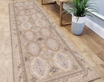 May include: A rectangular beige runner rug with an intricate geometric pattern. The rug features a border design and repeating octagonal and diamond shapes in shades of beige, blue, and pink. The rug is placed on a wooden floor.