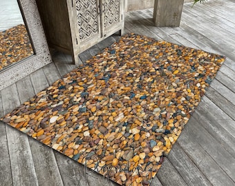 Può includere: Tappeto rettangolare con un motivo di ciottoli multicolori nei toni del marrone, giallo, blu e bianco. Il tappeto è posizionato su una superficie in legno. Il design del tappeto imita l'aspetto della pietra naturale, adatto per uso interno o esterno.
