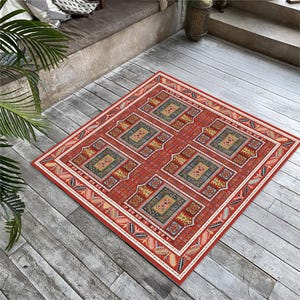 Könnte beinhalten: Ein quadratischer, roter Teppich mit einem aufwendigen geometrischen Muster. Der Teppich zeigt ein zentrales Design aus sich wiederholenden Quadraten in Blau-, Gelb- und Grüntönen, umrahmt von einem detaillierten Rand mit cremefarbenen und roten Akzenten. Auf einer Holzterrasse platziert.