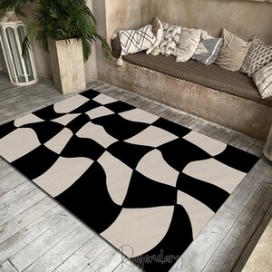 May include: A black and cream-colored area rug with a wavy checkerboard pattern. The rug is rectangular and lies on a wooden floor. The design features large, irregular squares in black and cream, creating a bold, modern look. The rug is suitable for a living room or bedroom.