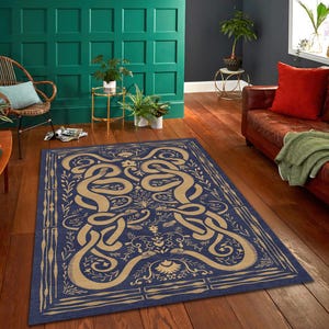 Op de afbeelding: Een rechthoekig vloerkleed met een marineblauwe achtergrond en een beige, verweven slangenontwerp. Het vloerkleed heeft bloemen- en bladmotieven, met een rand van verticale lijnen en bladeren. Het vloerkleed ligt op een houten vloer.