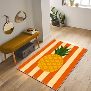 Può includere: Un tappeto rettangolare caratterizzato da una grande grafica centrale di un ananas giallo con foglie verdi. Lo sfondo è costituito da strisce verticali alternate in colori arancione brillante e crema, creando un motivo audace ad alto contrasto.