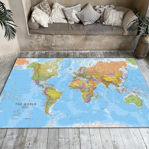 Pode incluir: Um tapete retangular com um design detalhado do mapa-múndi, mostrando países em várias cores contra um fundo azul oceânico. O tapete tem o texto "THE WORLD". O tapete está colocado em um chão de madeira.