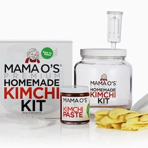 Puede incluir: Un kit de kimchi casero Mama O's Premium con un frasco de vidrio transparente, una tapa blanca, un frasco rojo de pasta de kimchi y una caja blanca con el texto "Mama O's Premium Homemade Kimchi Kit" impreso en él.