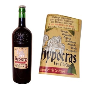 Op de afbeelding: Een fles rode wijn met het etiket "Vin Médiéval Hypocras" met een middeleeuwse illustratie van een persoon die wijn maakt. De fles staat naast een gevouwen folder met hetzelfde etiket en tekst die de ingrediënten en de bereiding van de wijn beschrijft.