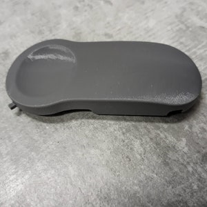 Peut inclure: Une pièce de voiture en plastique gris de forme arrondie avec un petit trou sur le côté.