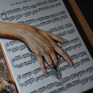Può includere: Un dipinto su tela che raffigura una mano appoggiata su uno spartito musicale intitolato The Heart Asks Pleasure First di Michael Nyman. La mano sembra sollevare il foglio, creando un effetto tridimensionale sulla superficie bianca.
