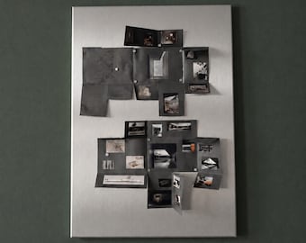 Puede incluir: Un tablero magnético rectangular de metal plateado que presenta una colección de fotografías en blanco y negro y bocetos arquitectónicos dispuestos en un collage, fijados a la superficie con pequeños imanes circulares.