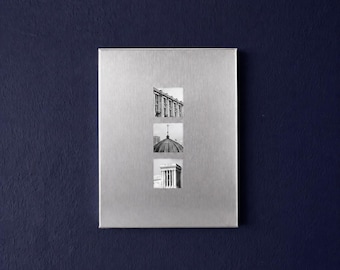 May include: A rectangular brushed silver metal wall plaque featuring three vertically aligned square black and white photographs. The top image shows a building facade, the middle shows a domed roof with a cross, and the bottom shows a building.